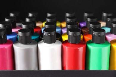 Photo of Acrylic paints of different colors in bottles against black background, closeup