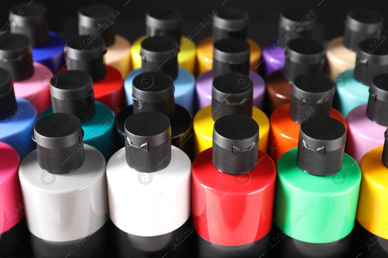 Photo of Acrylic paints of different colors in bottles against black background, closeup