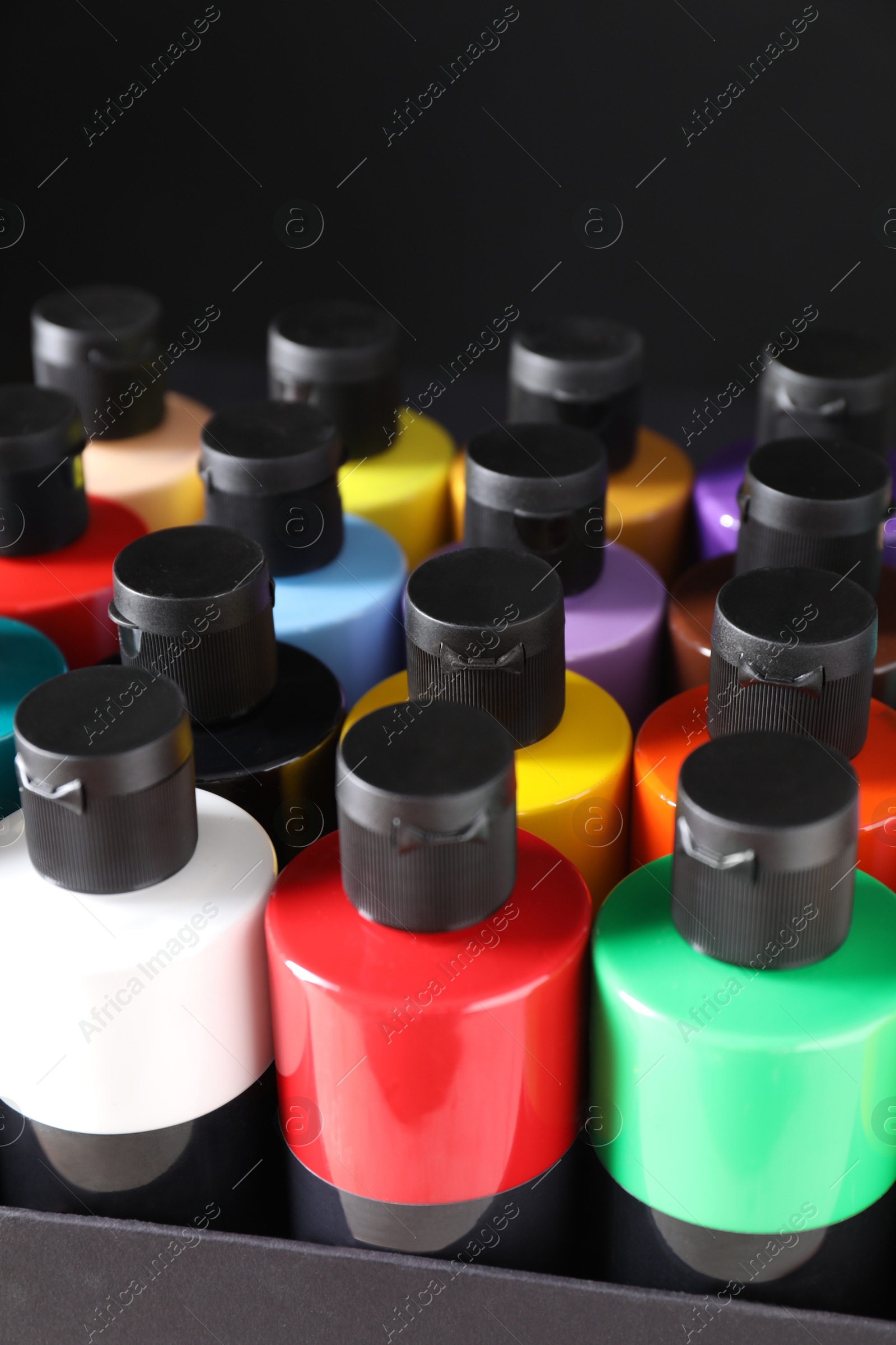 Photo of Acrylic paints of different colors in bottles against black background, closeup