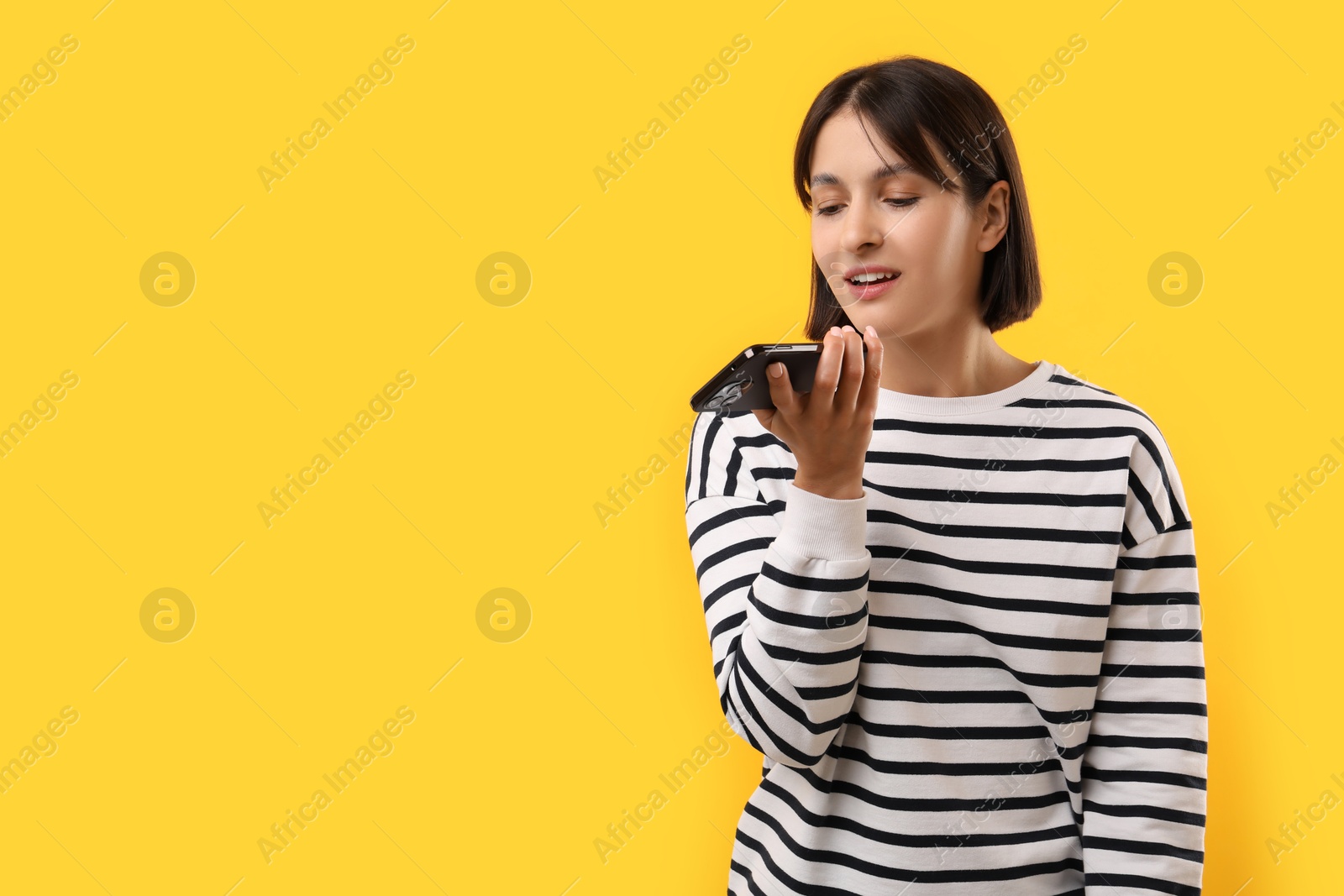 Photo of Beautiful woman recording voice message via smartphone on yellow background, space for text