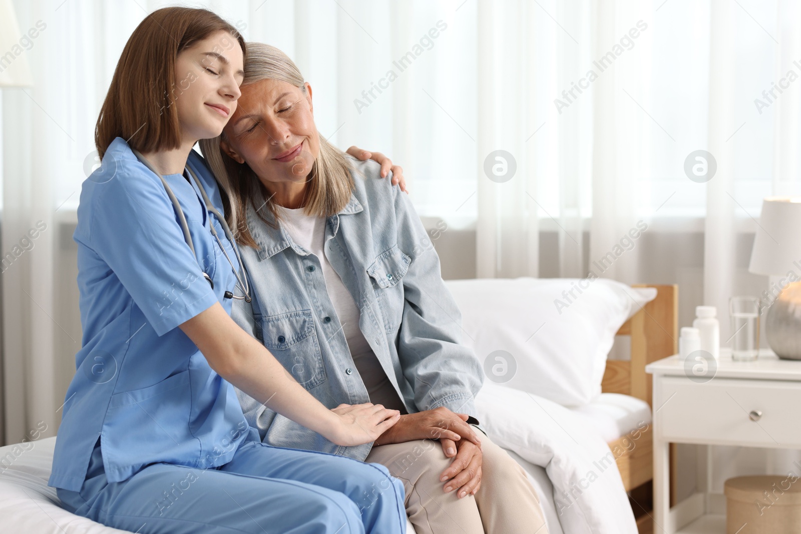 Photo of Young healthcare worker supporting senior patient on bed indoors. Space for text