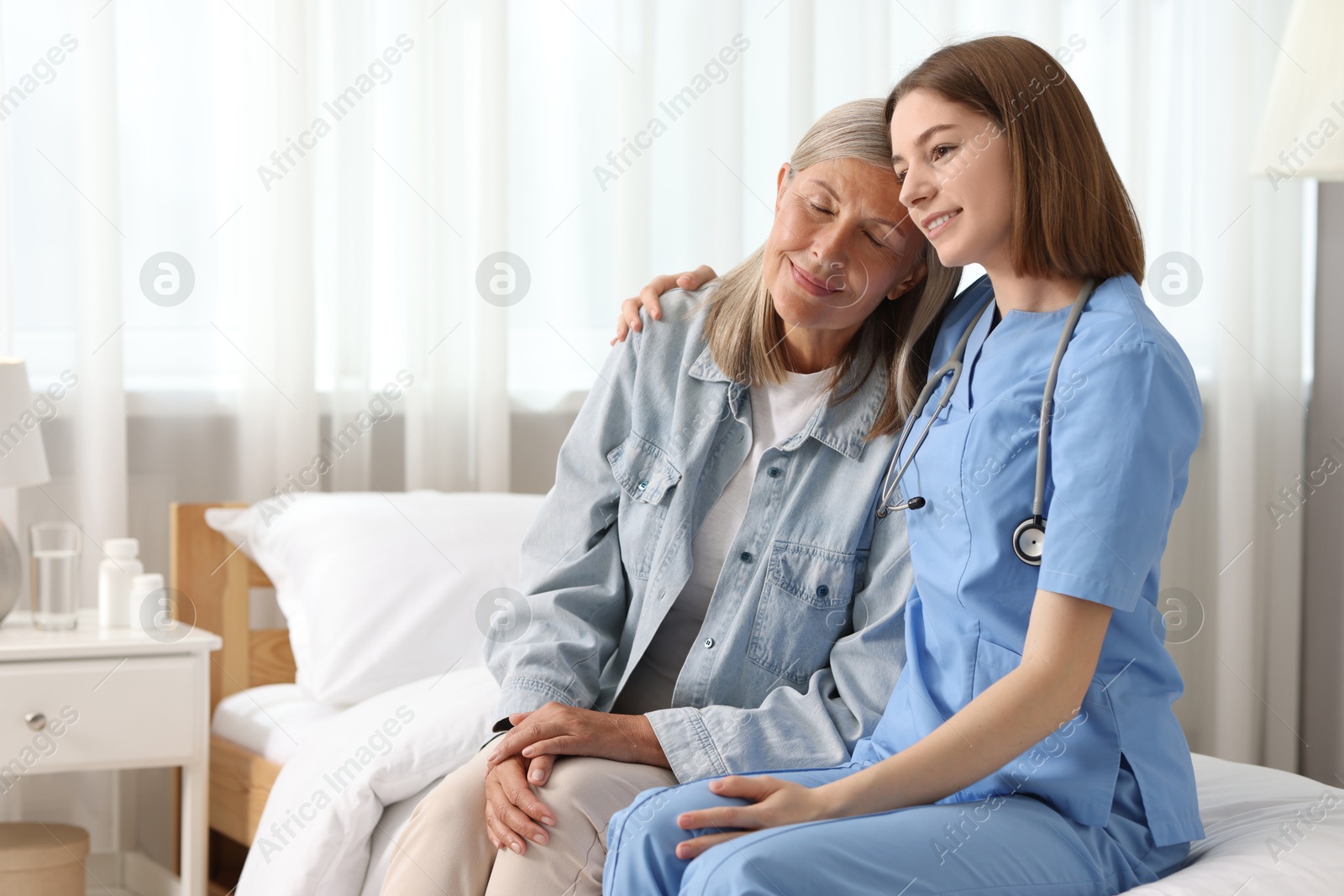 Photo of Smiling healthcare worker supporting senior patient on bed indoors. Space for text