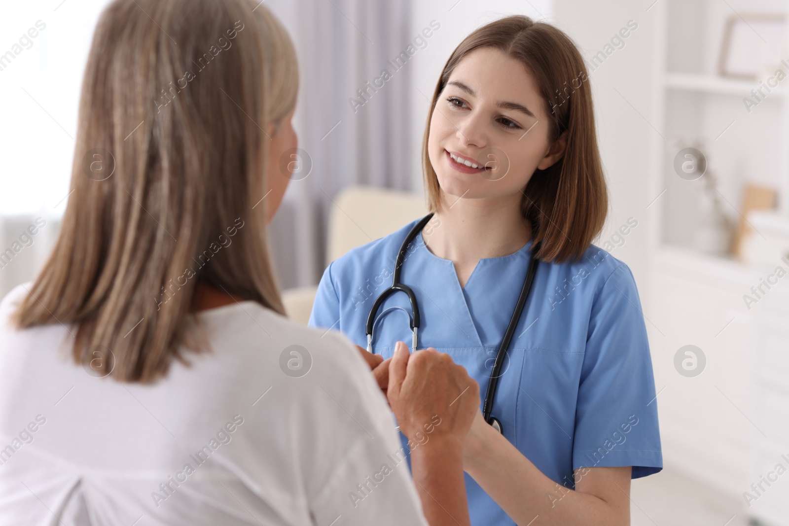 Photo of Smiling healthcare worker in uniform supporting patient indoors, back view