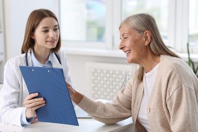 Smiling healthcare worker and senior patient checking clipboard with analysis results in hospital