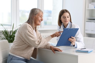 Smiling healthcare worker and senior patient checking clipboard with analysis results in hospital