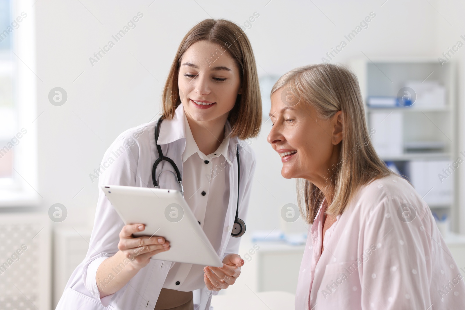 Photo of Smiling healthcare worker and senior patient checking analysis results on tablet in hospital