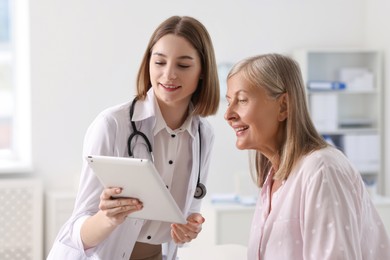 Photo of Smiling healthcare worker and senior patient checking analysis results on tablet in hospital