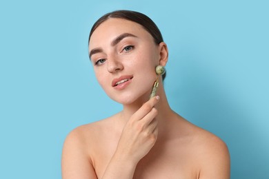 Photo of Beautiful young woman doing facial massage with roller on light blue background