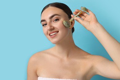 Beautiful young woman doing facial massage with roller on light blue background