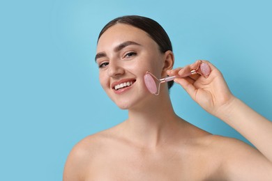 Photo of Beautiful young woman doing facial massage with roller on light blue background