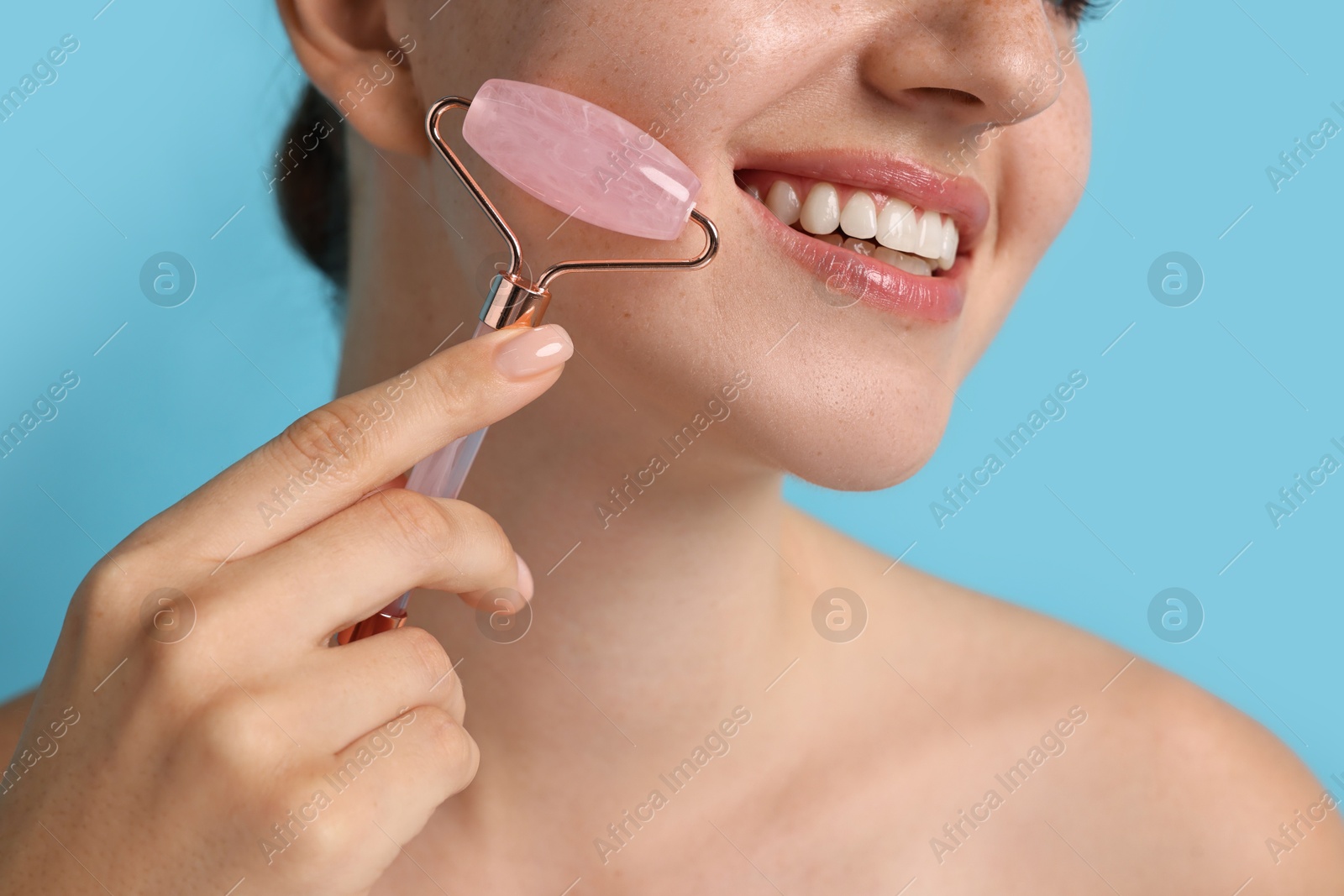 Photo of Woman doing facial massage with roller on light blue background, closeup