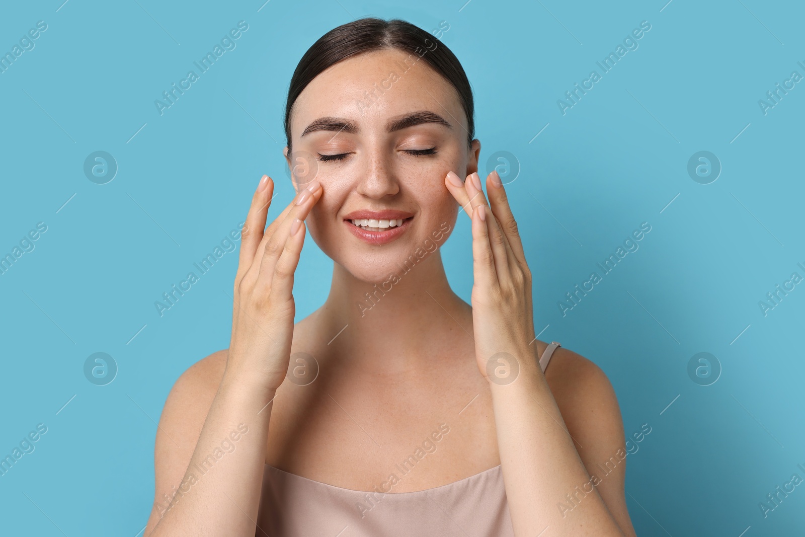 Photo of Beautiful young woman doing facial massage on light blue background