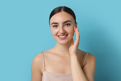 Beautiful young woman with healthy skin on light blue background