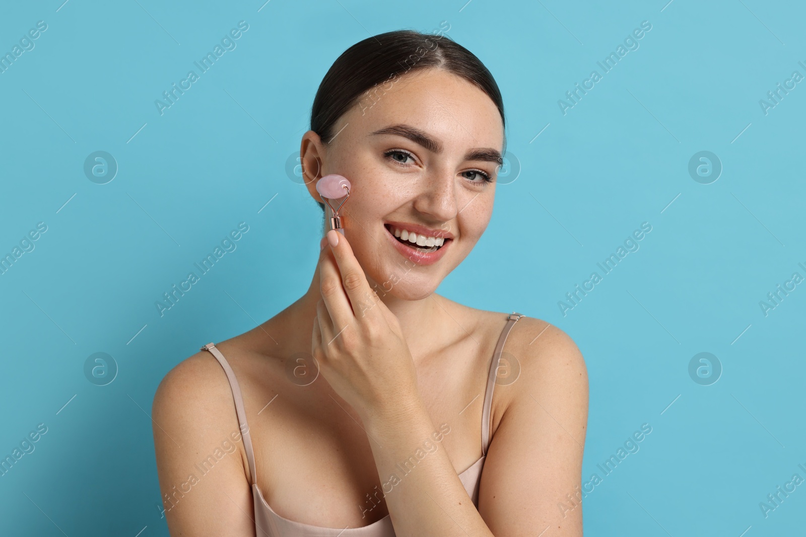 Photo of Beautiful young woman doing facial massage with roller on light blue background