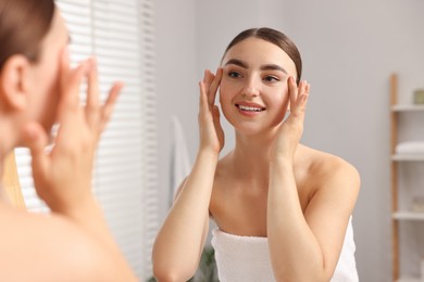 Photo of Beautiful young woman doing facial massage near mirror at home