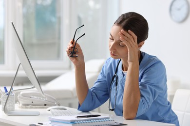 Tired nurse with glasses at white table in clinic