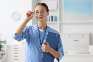 Nurse in medical uniform with clipboard indoors, space for text