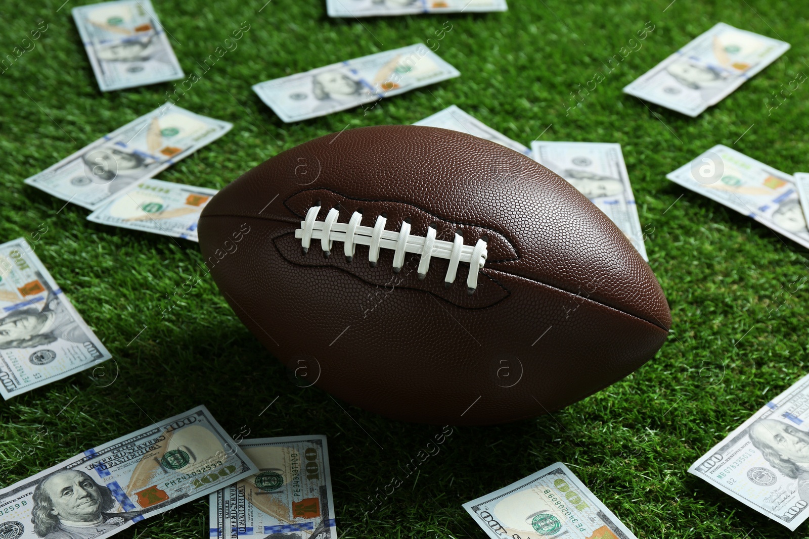 Photo of American football ball and dollar banknotes on green grass outdoors