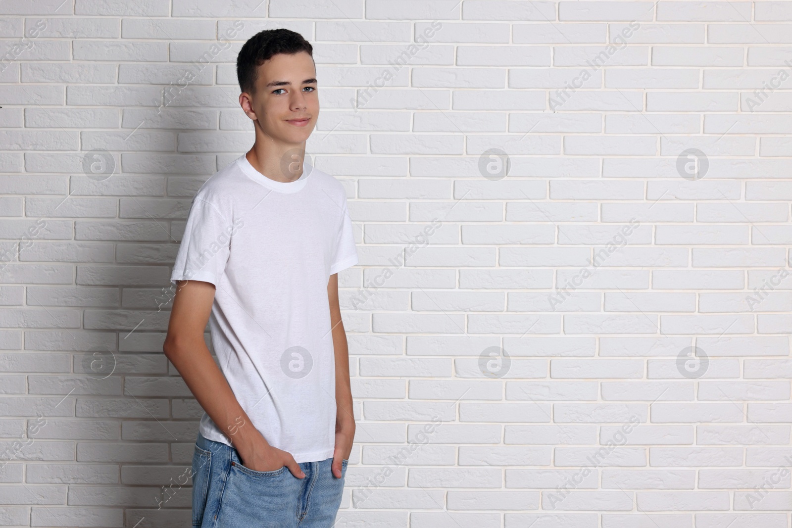 Photo of Teenage boy wearing t-shirt near white brick wall, space for text