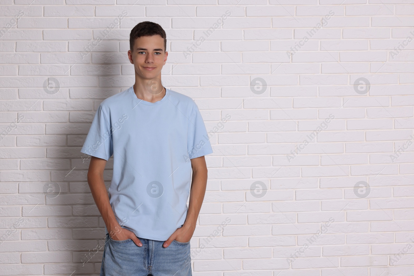 Photo of Teenage boy wearing light blue t-shirt near white brick wall, space for text