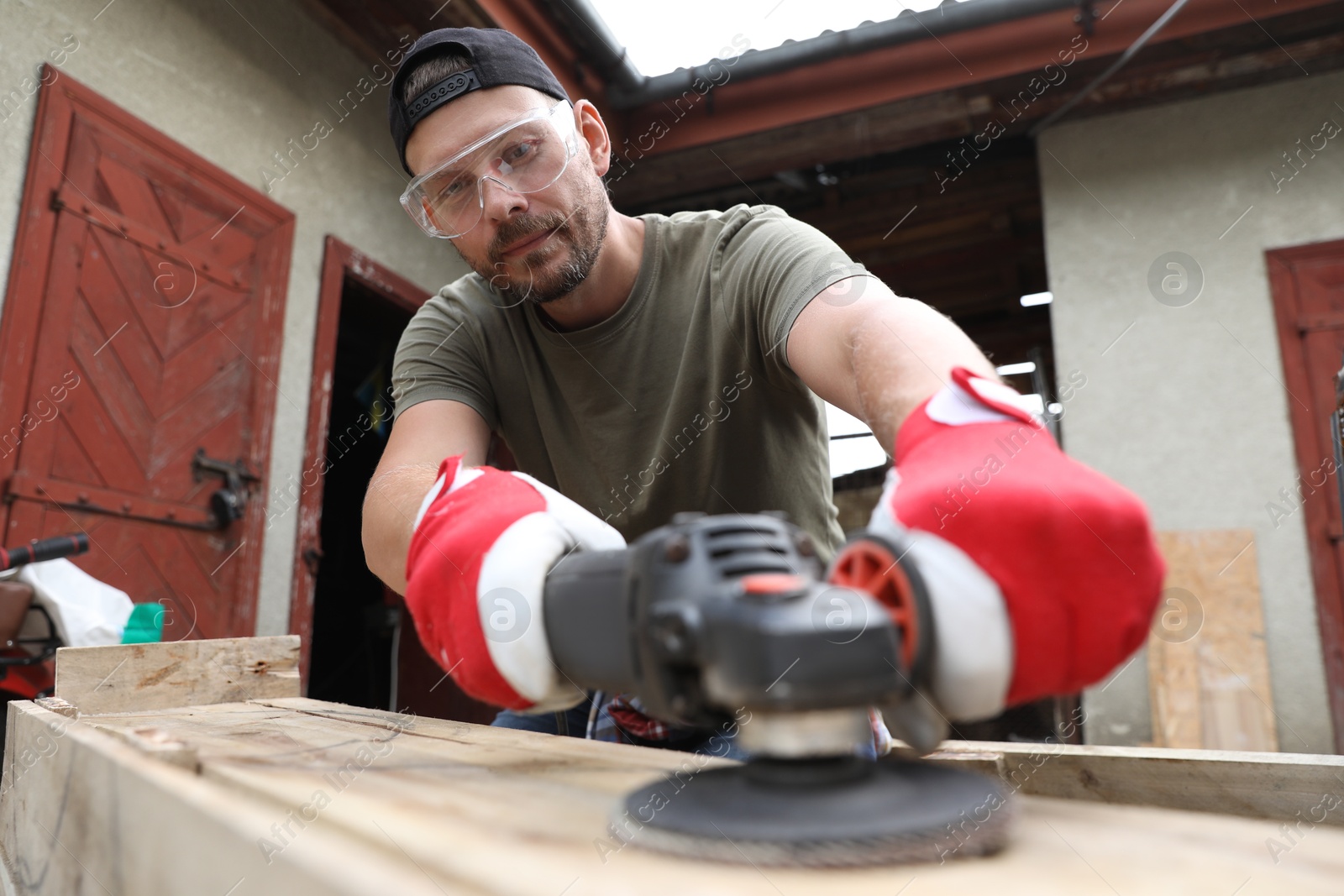 Photo of Man polishing wooden planks with angle grinder outdoors