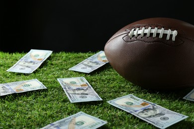 Photo of American football ball and dollar banknotes on green grass