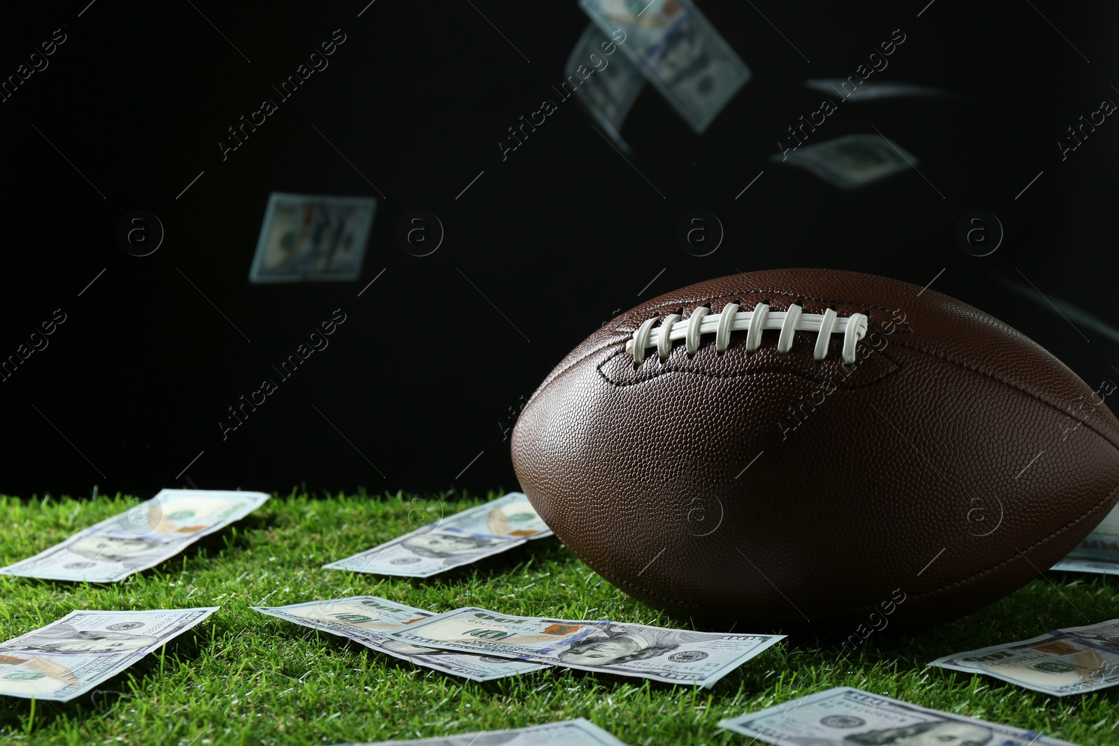 Photo of American football ball and dollar banknotes on green grass