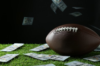 Photo of American football ball and dollar banknotes on green grass