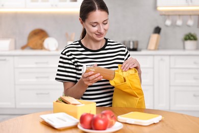 Smiling woman preparing lunch box with healthy snacks at wooden table in kitchen