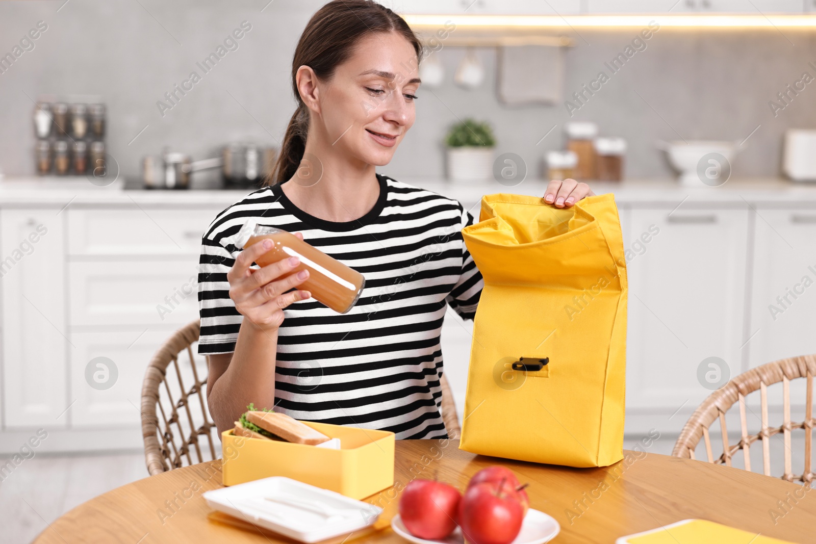 Photo of Smiling woman preparing lunch box with healthy snacks at wooden table in kitchen