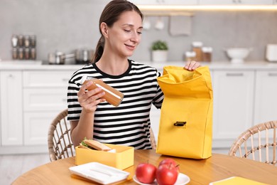 Smiling woman preparing lunch box with healthy snacks at wooden table in kitchen