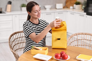 Photo of Smiling woman preparing lunch box with healthy snacks at wooden table in kitchen