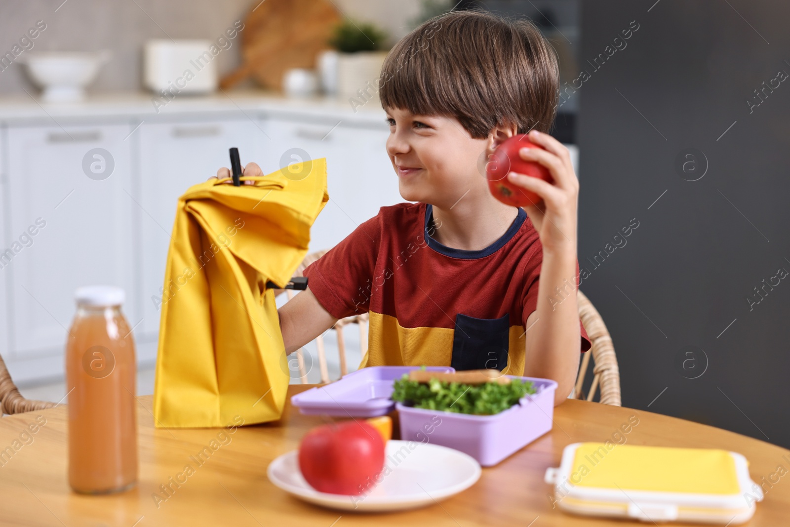 Photo of Cute boy with lunch box, healthy products and bag at wooden table in kitchen