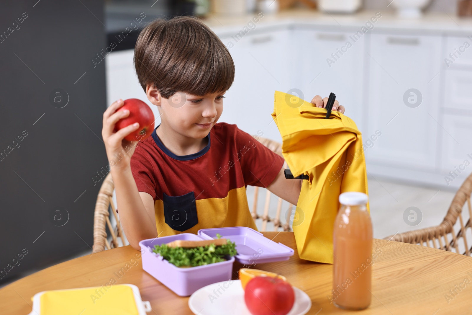 Photo of Cute boy with lunch box, healthy products and bag at wooden table in kitchen