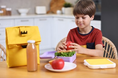 Cute boy with lunch box, healthy products and bag at wooden table in kitchen