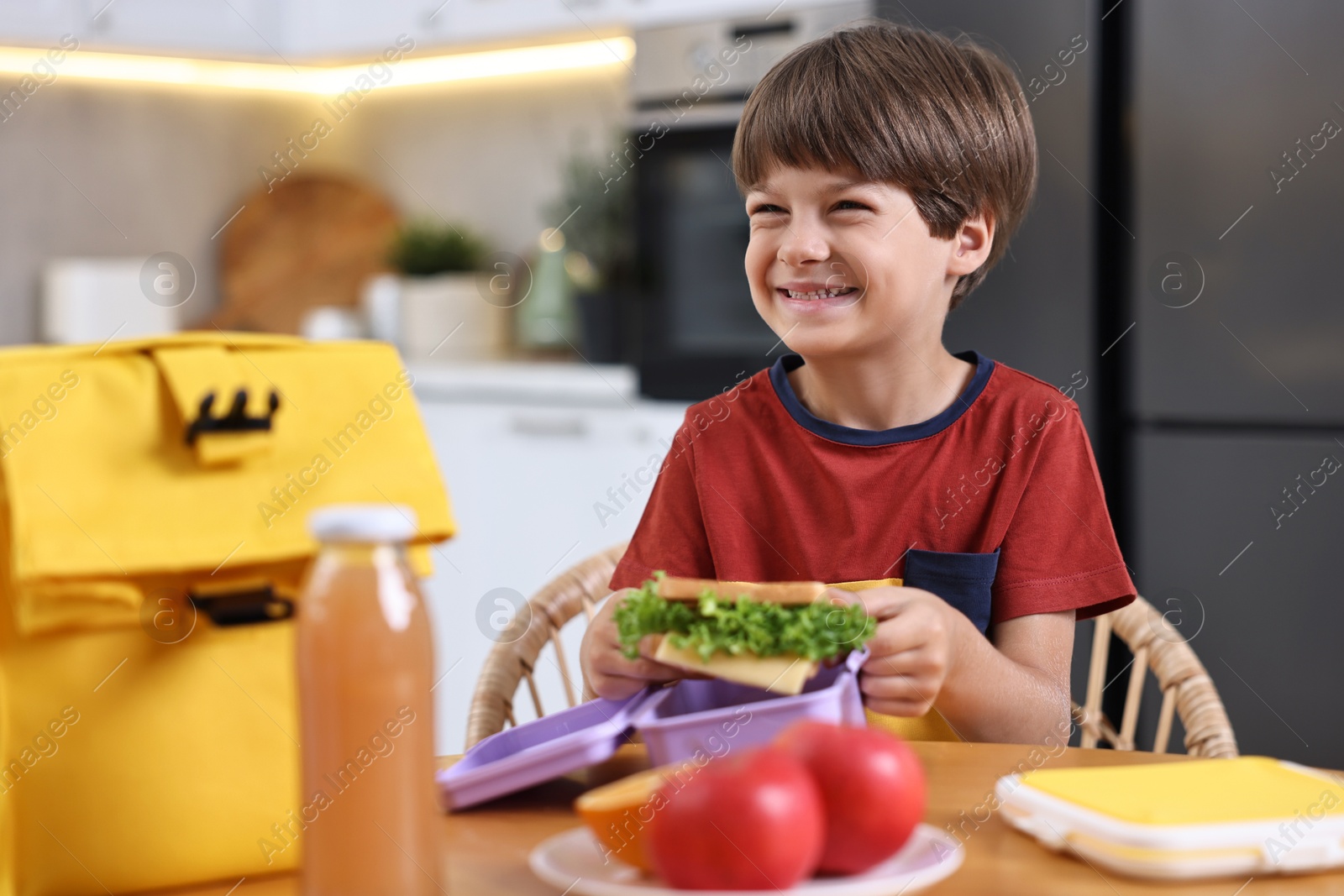 Photo of Cute boy with lunch box, healthy products and bag at wooden table in kitchen