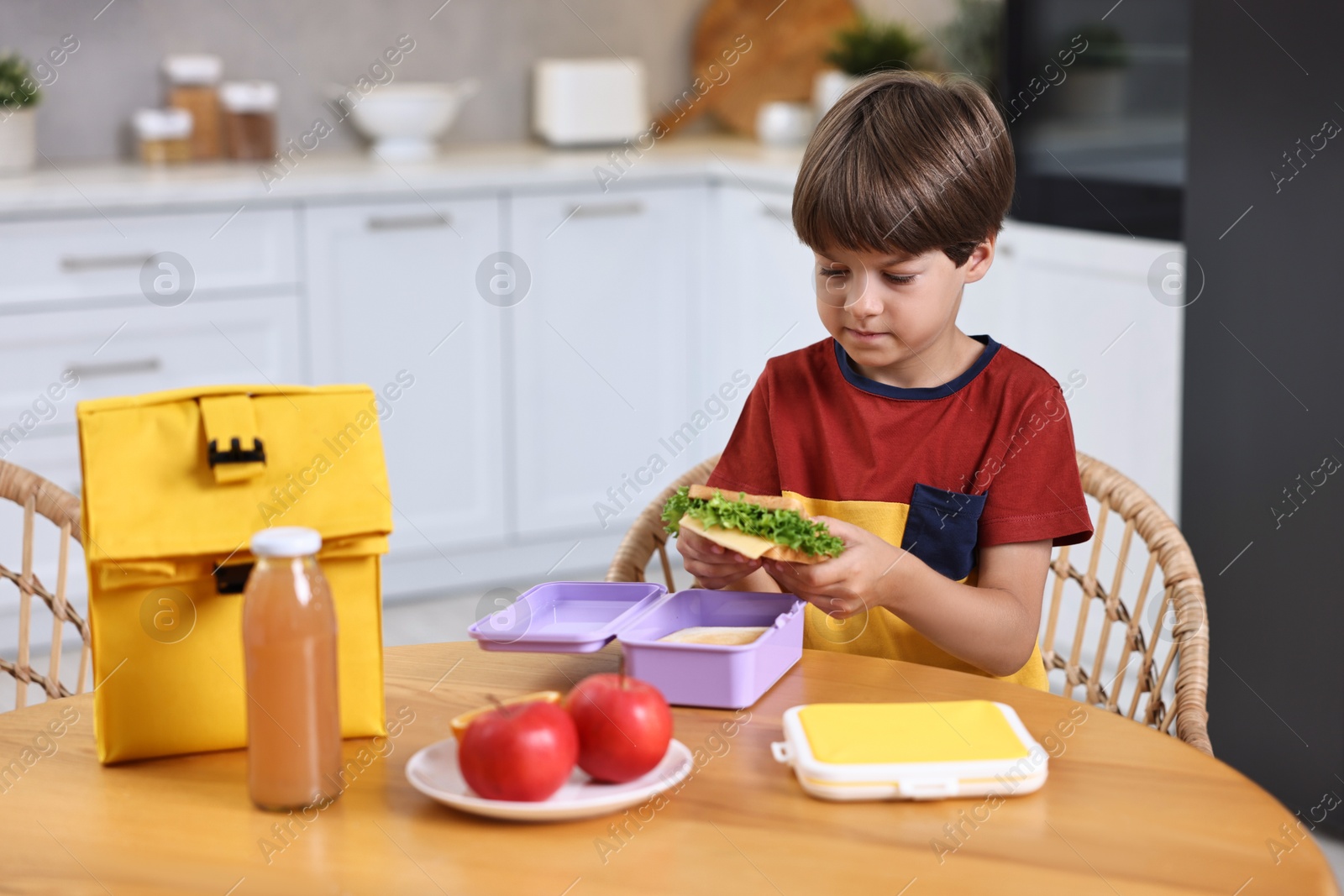 Photo of Cute boy with lunch box, healthy products and bag at wooden table in kitchen