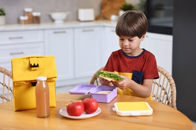 Cute boy with lunch box, healthy products and bag at wooden table in kitchen