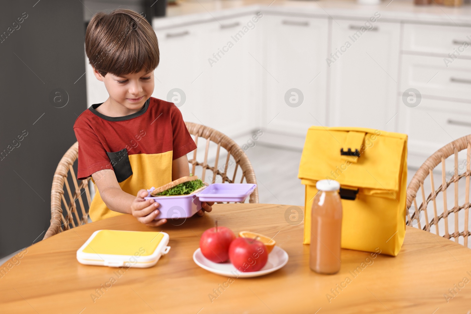 Photo of Cute boy with lunch box, healthy products and bag at wooden table in kitchen