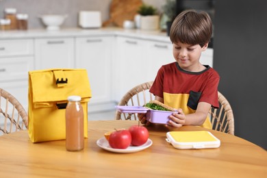 Photo of Cute boy with lunch box, healthy products and bag at wooden table in kitchen