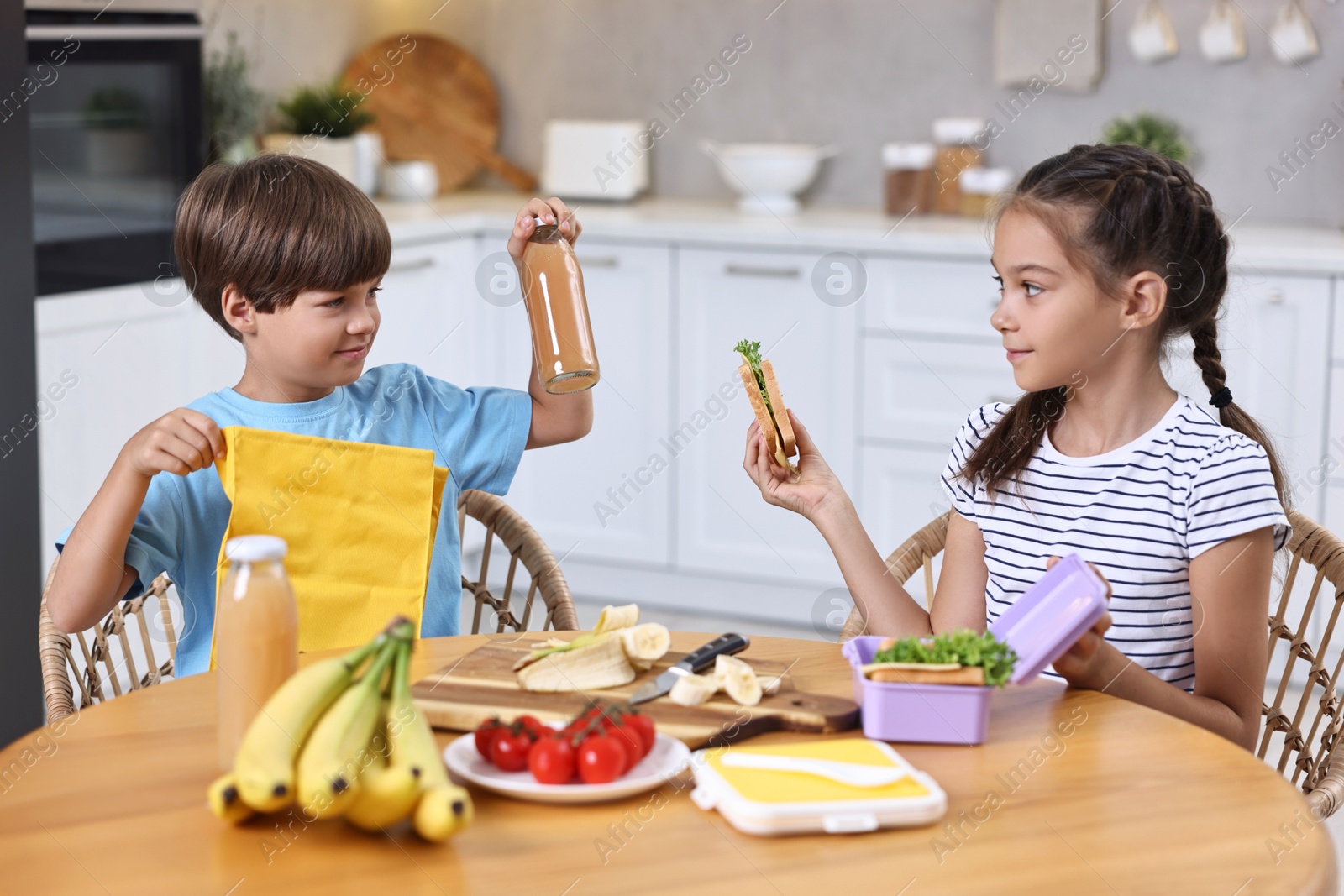 Photo of Cute children with healthy snacks preparing lunch box at wooden table in kitchen