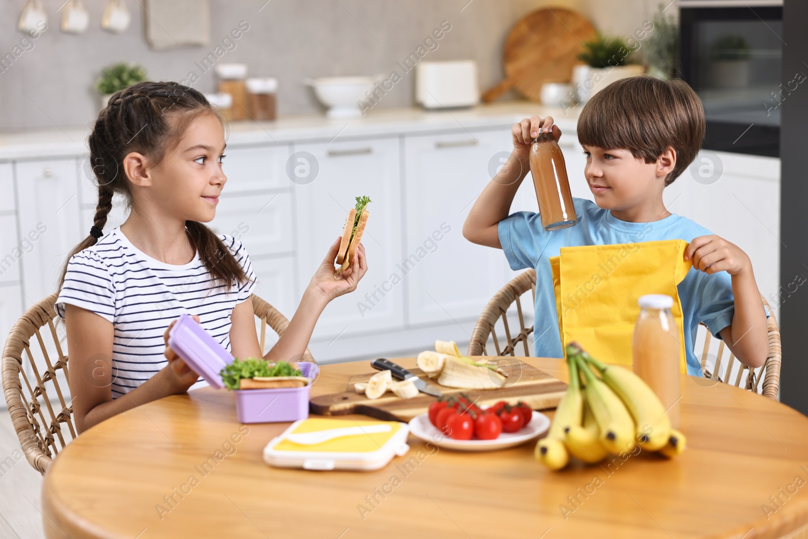 Photo of Cute children with healthy snacks preparing lunch box at wooden table in kitchen