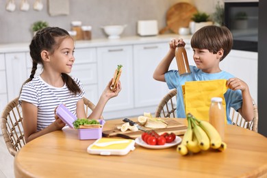 Cute children with healthy snacks preparing lunch box at wooden table in kitchen