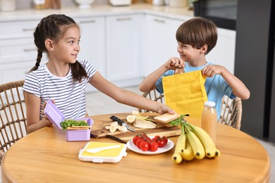 Photo of Cute children with healthy snacks preparing lunch box at wooden table in kitchen