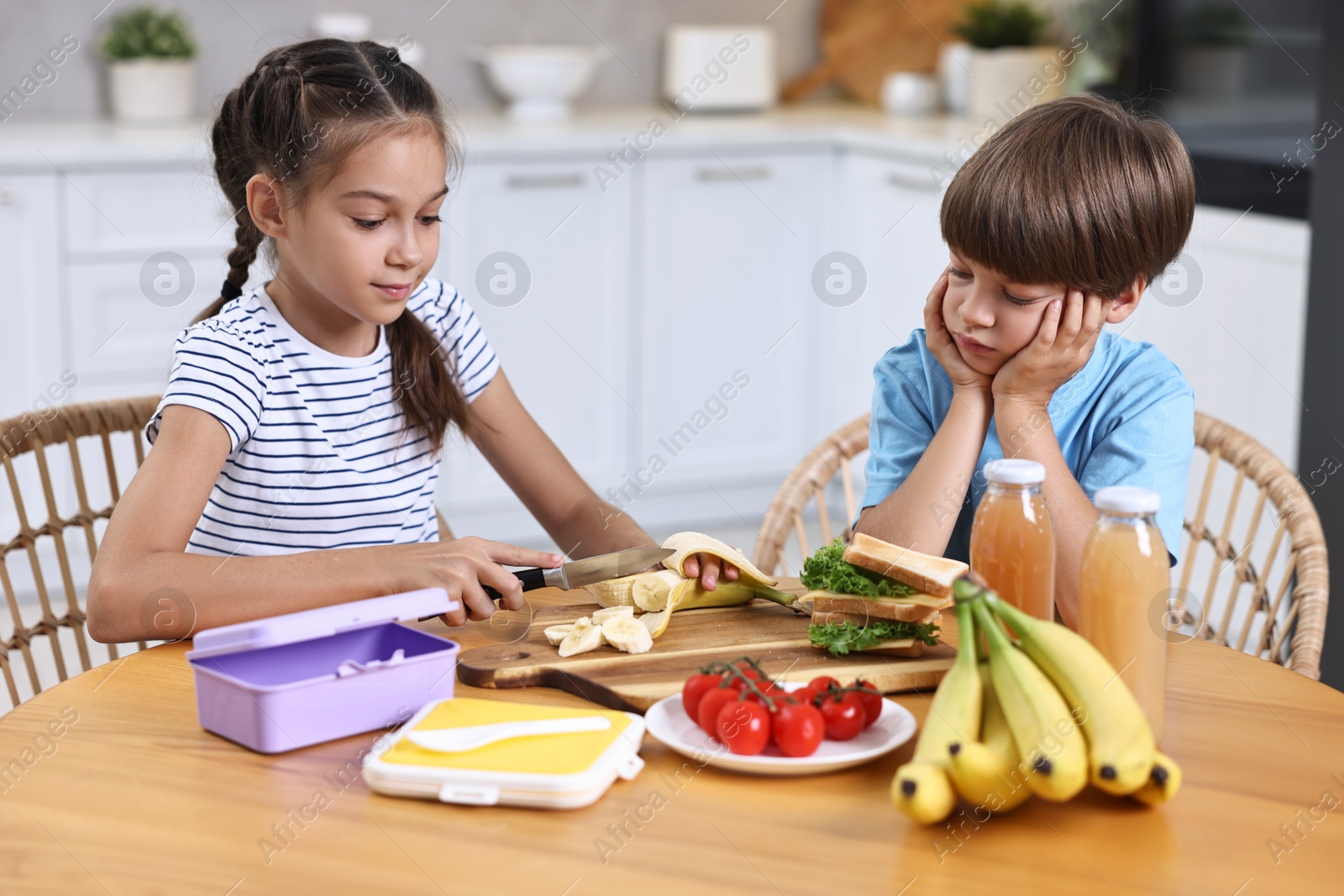 Photo of Cute children with healthy snacks preparing lunch box at wooden table in kitchen