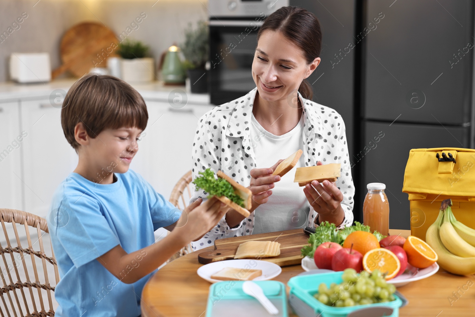 Photo of Mother and her cute son preparing lunch box with healthy food at wooden table in kitchen