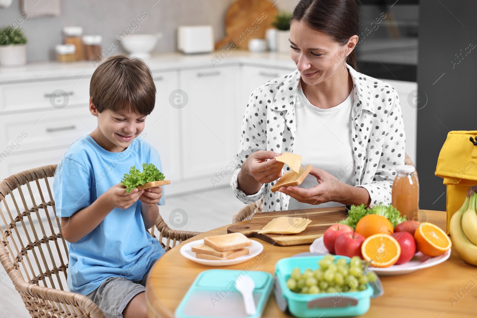 Photo of Mother and her cute son preparing lunch box with healthy food at wooden table in kitchen