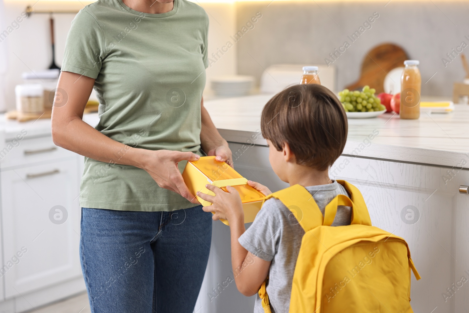 Photo of Mother giving lunch box to her son in kitchen, closeup