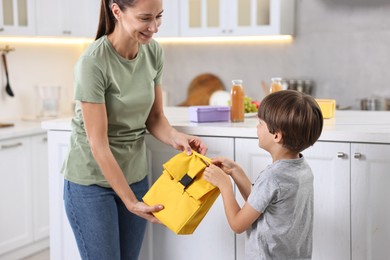 Smiling mother giving lunch bag to her son in kitchen