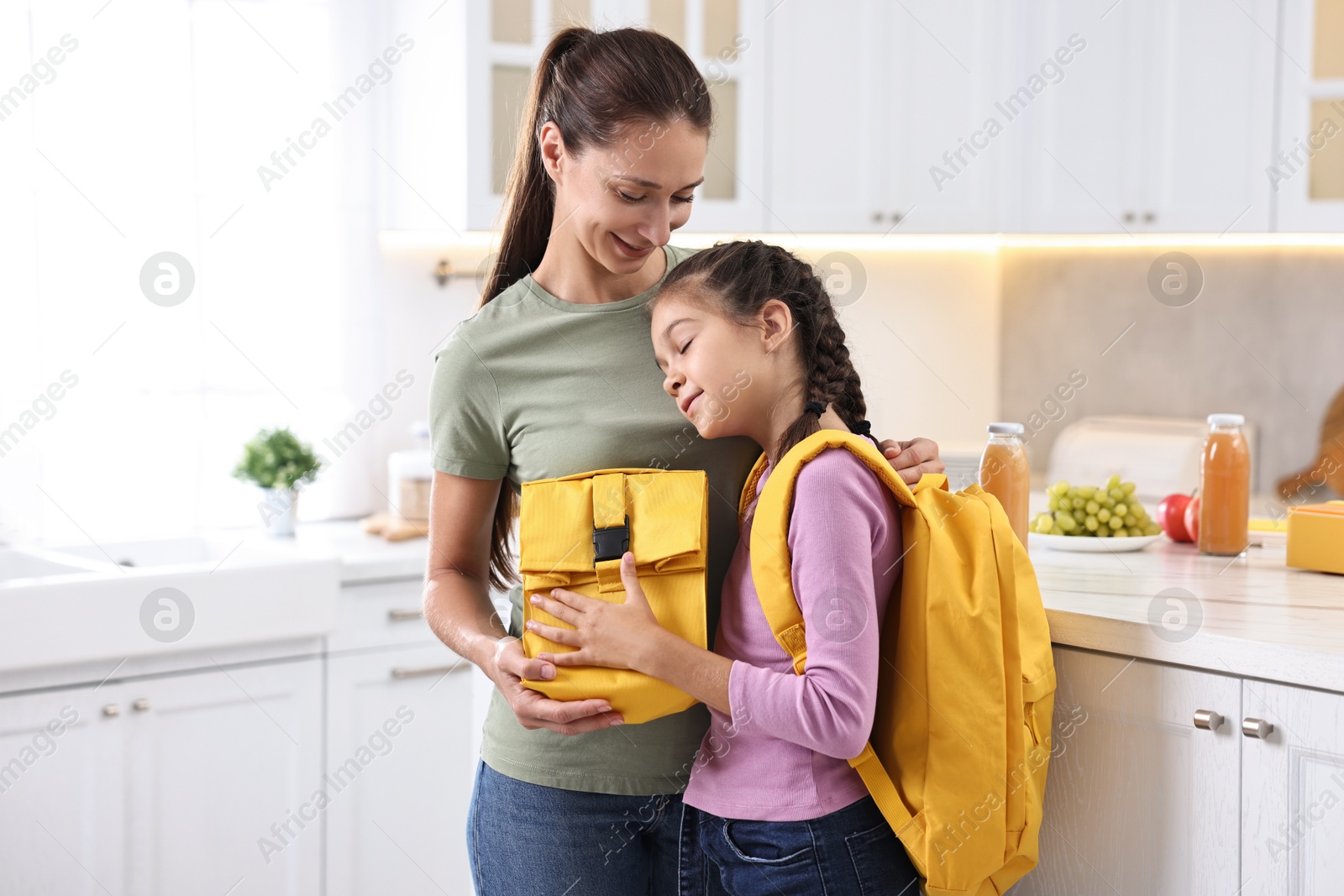 Photo of Smiling mother and her daughter with lunch bag in kitchen. Preparing for school